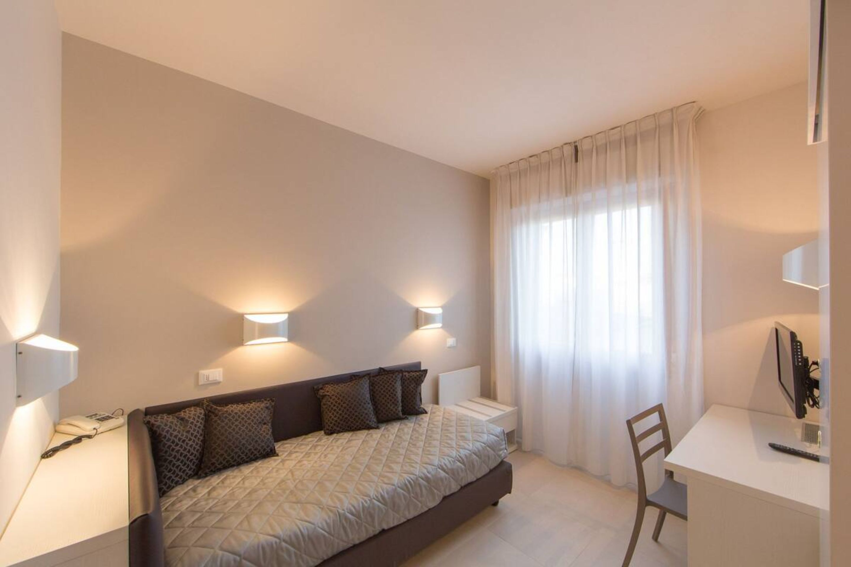 Un dormitorio con cama, lámparas de noche, un escritorio y una silla.