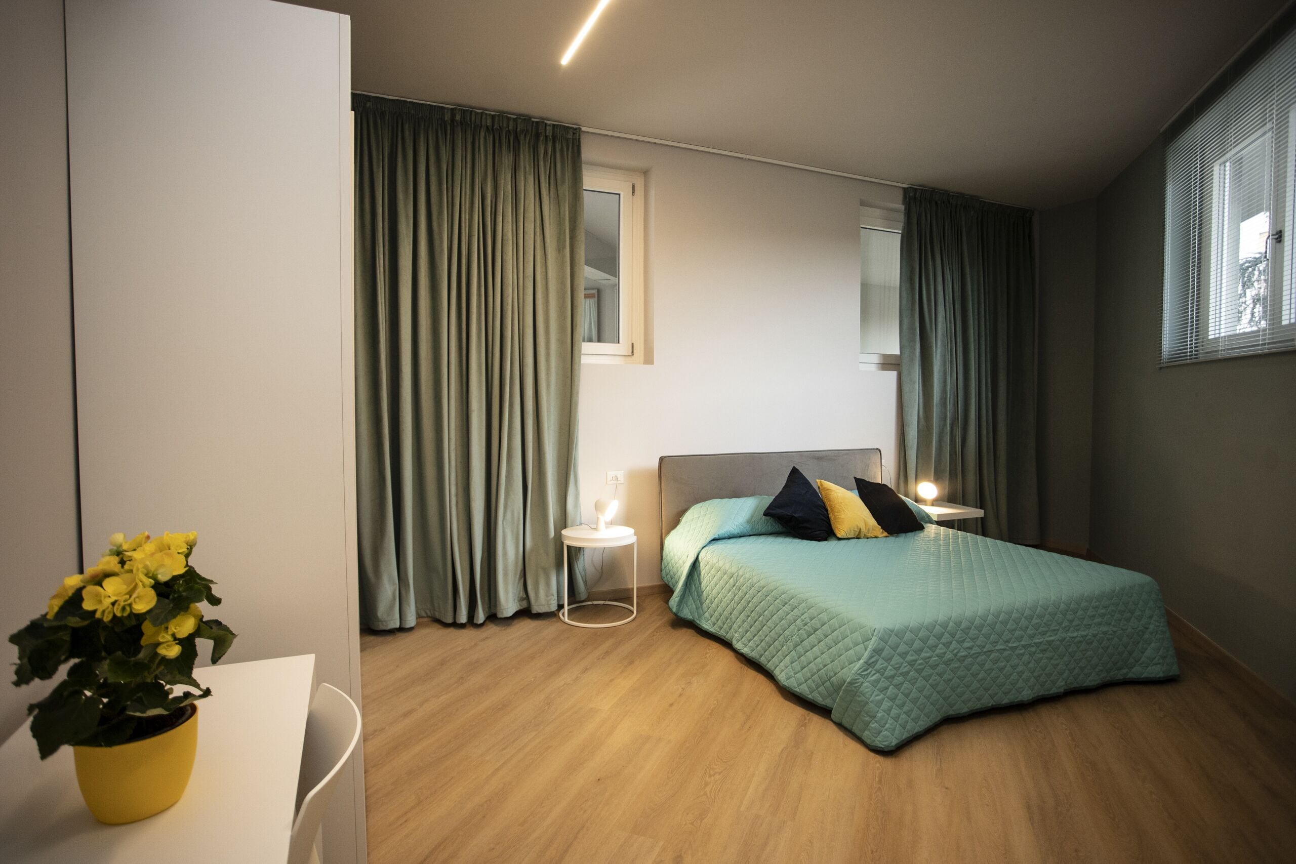 Un dormitorio moderno con cama, mesitas de noche, una planta en maceta y cortinas.