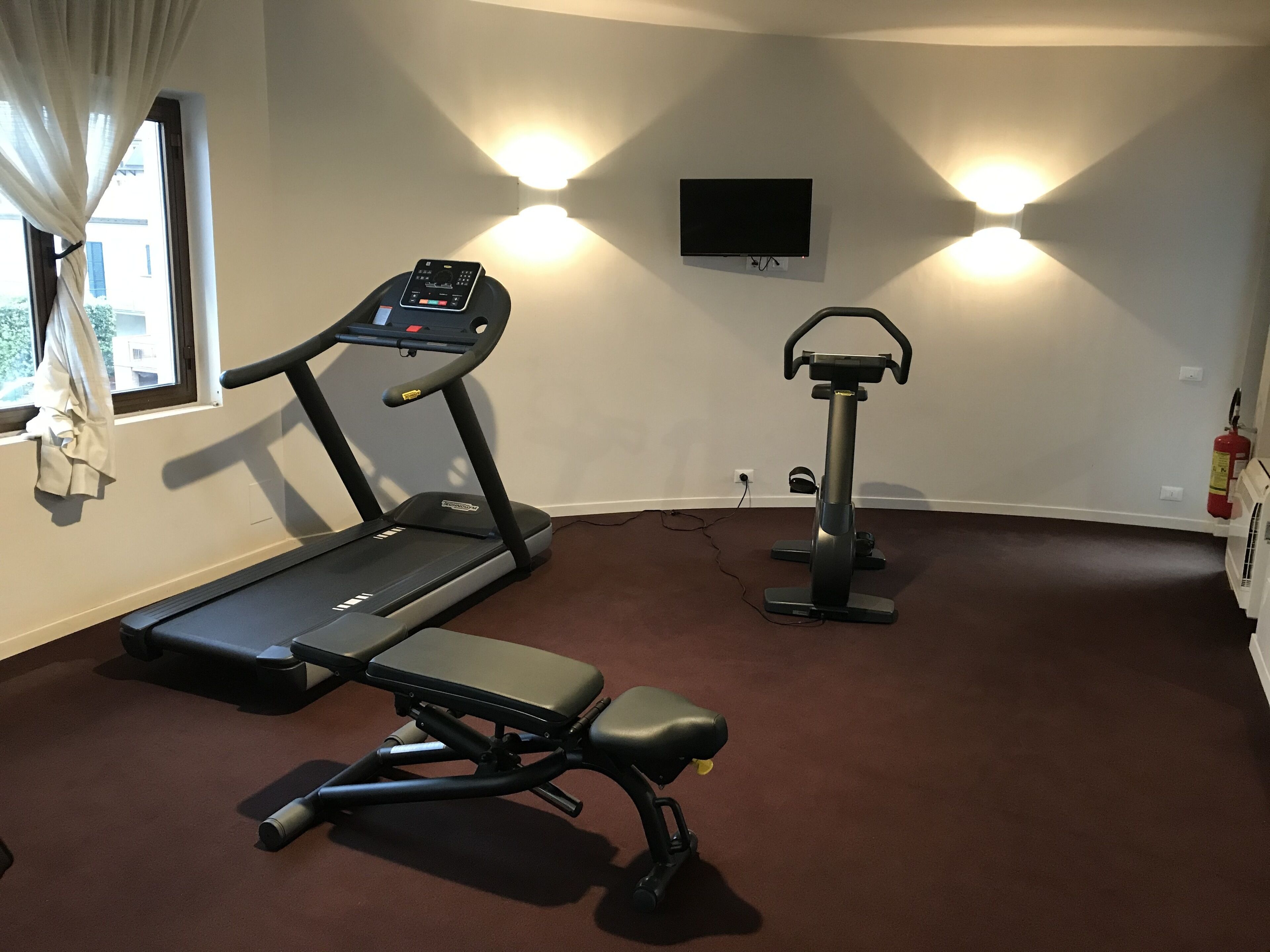 A home gym with a treadmill, a stationary bike, and a bench.