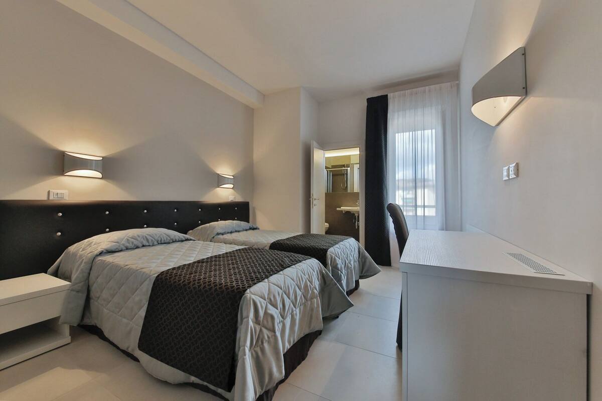 A modern hotel room with two beds, a desk, and a bathroom visible through an open door.