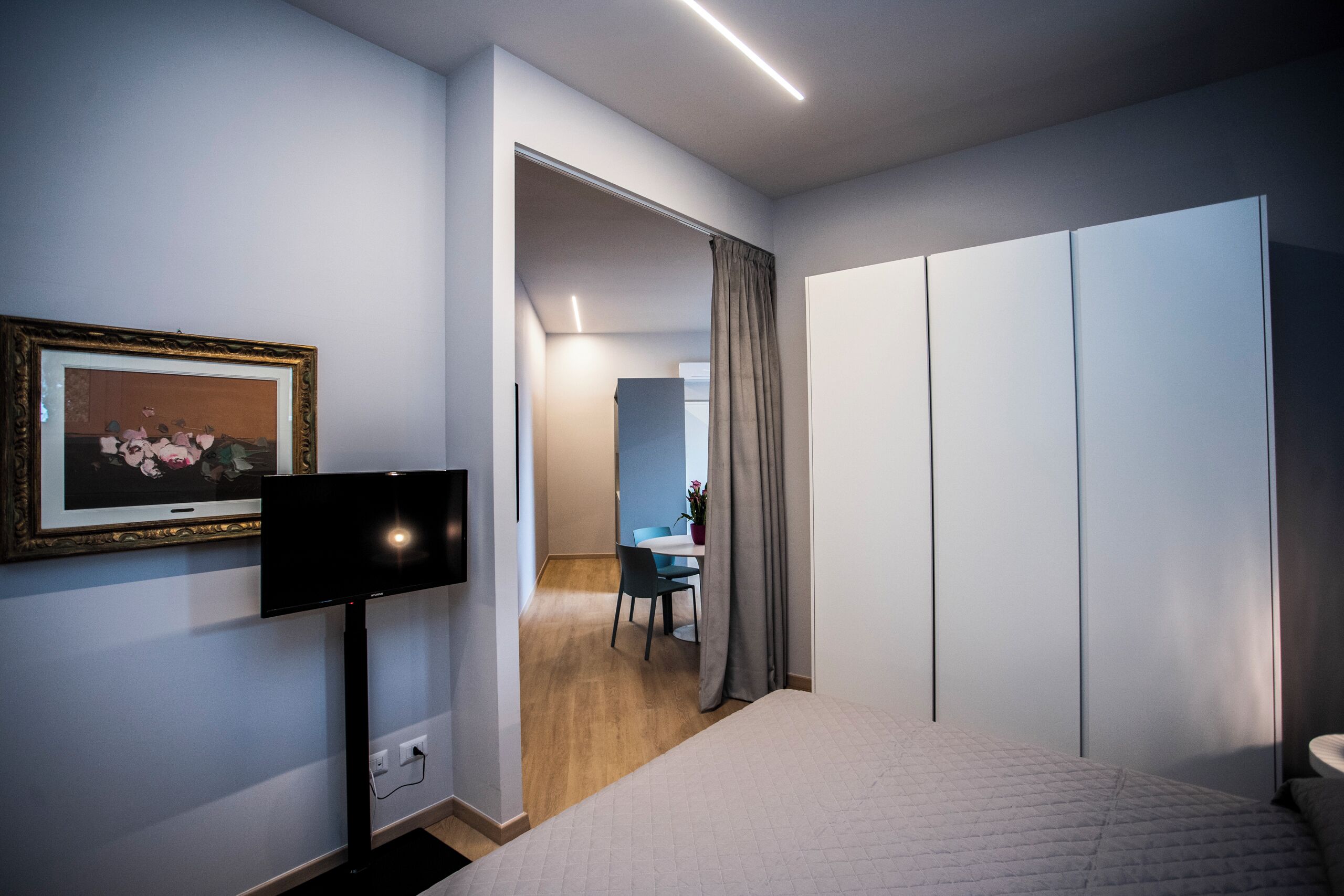 Ein modernes Hotelzimmer mit einem Bett, einem Flachbildfernseher, einem gerahmten Bild an der Wand, einem Schreibtisch mit Stuhl und einem Kleiderschrank.