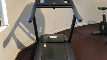 Una cinta de correr en una habitación con un televisor montado en la pared y una ventana a la izquierda.