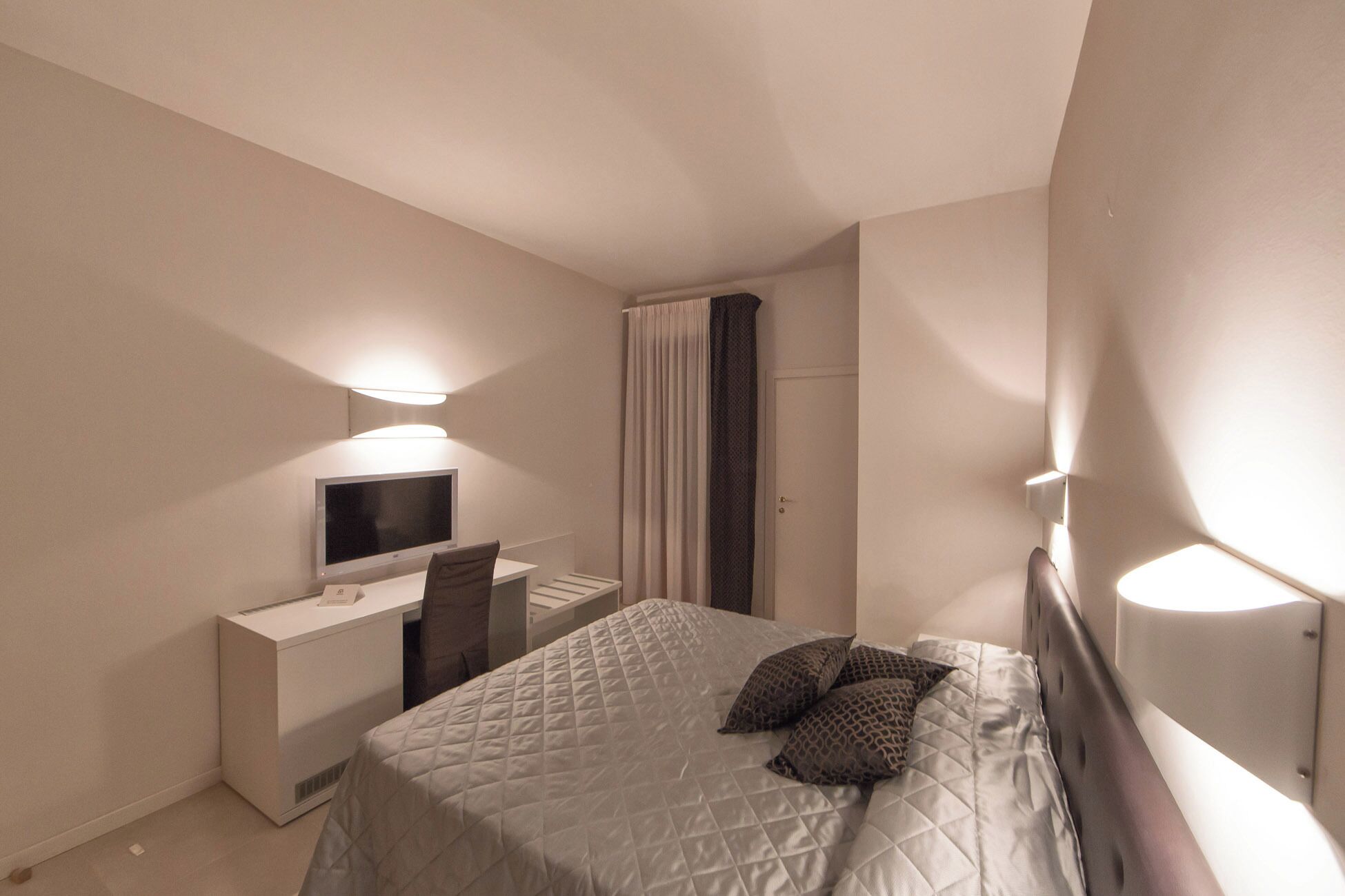 Ein Schlafzimmer mit einem Bett, einem Schreibtisch, einem Stuhl, einem Fernseher und einer Tür.