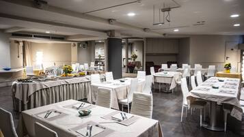 A spacious dining area with multiple round tables, each set with white tablecloths, chairs, and neatly arranged cutlery.