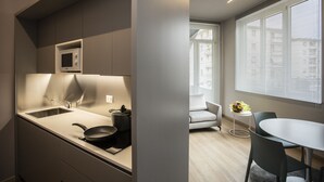 A modern kitchen with a built-in microwave, sink, and stove. There is a dining area with a table and chairs, and a window with blinds. - Delta Hotel (Montevarchi)