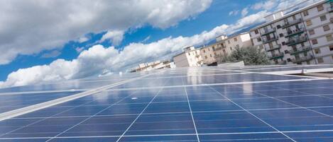 Eine Anordnung von Solarmodulen vor blauem Himmel und Gebäuden im Hintergrund.