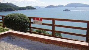 A wooden deck overlooking a body of water with a sign in a foreign language, a clear view of the water, and distant islands.