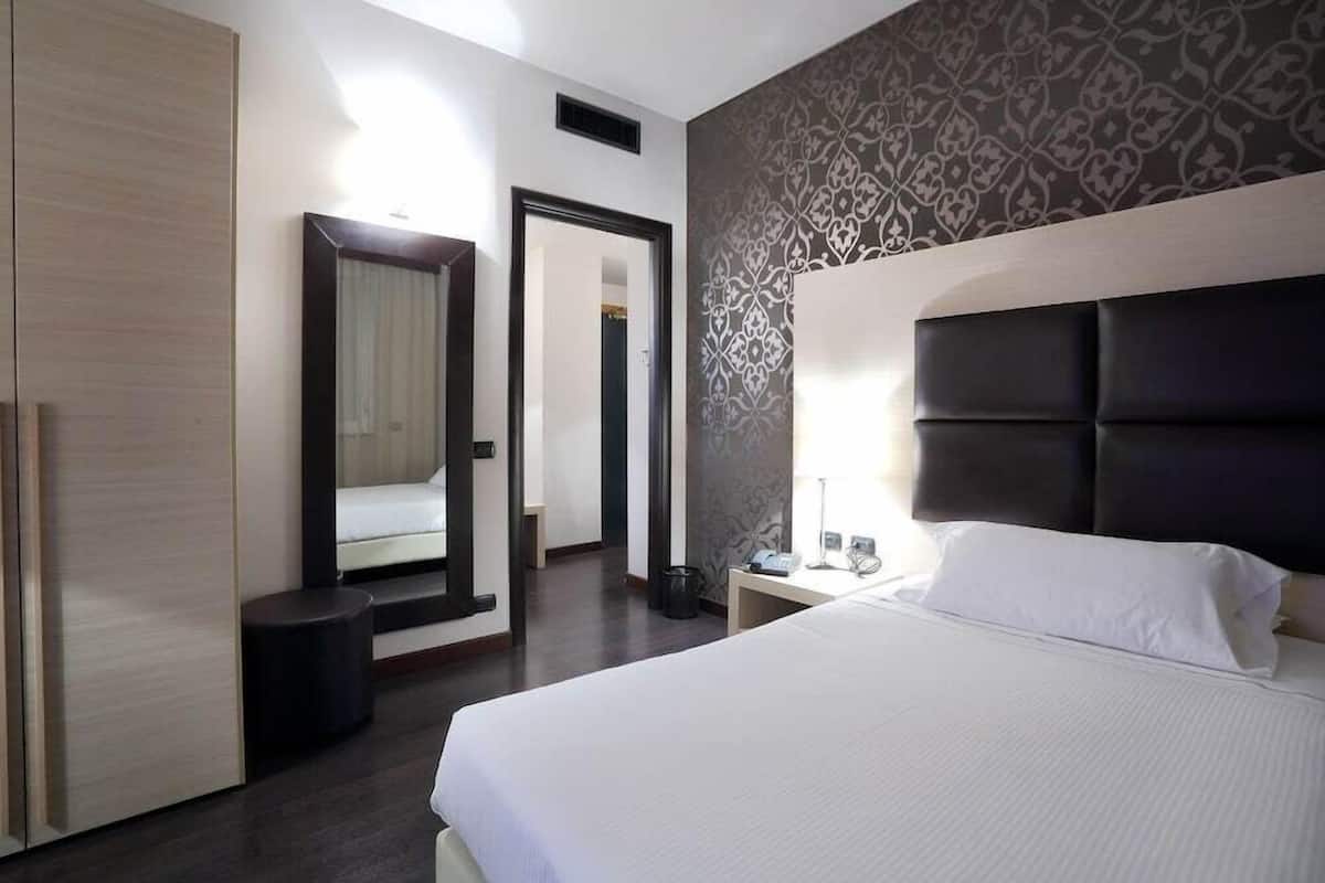 Una camera d'albergo con un letto, un armadio, uno specchio e una parete decorata.
