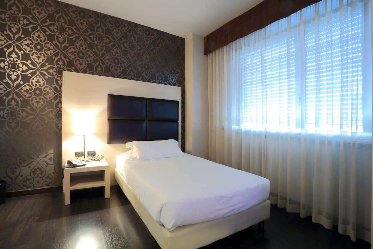 Una camera d'albergo con un letto, un comodino, una lampada e una finestra con tende.