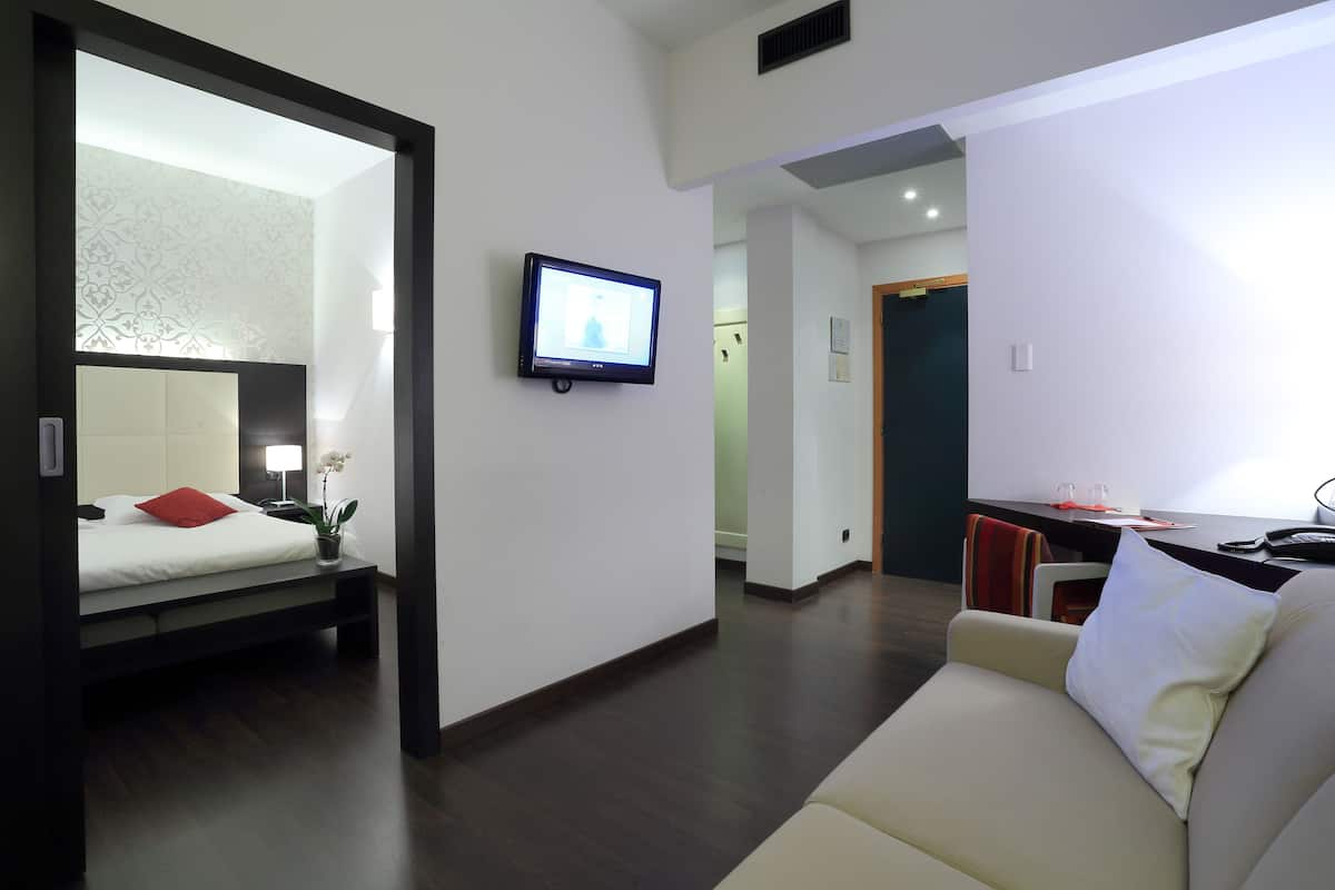 Una moderna camera d'albergo con un letto, una televisione, un divano e una scrivania con una sedia.