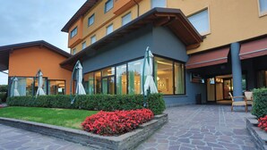 Um hotel com design moderno, com entrada em pedra, área de estar externa com guarda-sóis e um jardim bem cuidado com flores vermelhas.