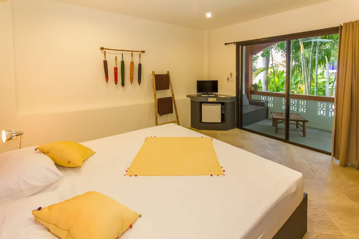 Habitación de hotel con cama, escritorio y vistas a la vegetación a través de una puerta corrediza.