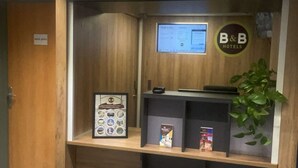 Een receptiebalie met een logo van een B&B, een digitaal scherm, een ingelijste foto en een plant.