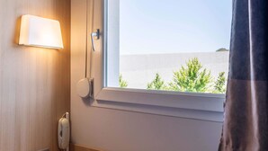Hotelkamer met een bedtelefoon, een wandlamp en een raam met uitzicht op groen en een gebouw.