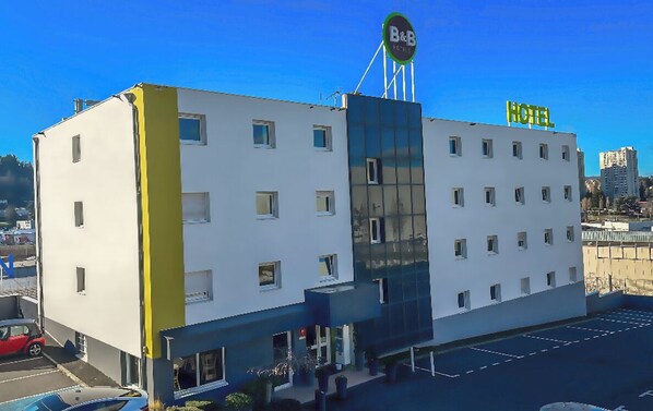 A modern hotel building with a prominent B&B sign, multiple windows, and a parking lot.