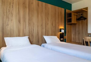 A hotel room with two beds, a wooden wall, a hanging coat rack, and a desk with a chair.