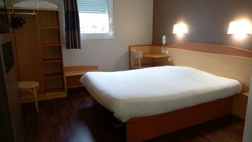 Una habitación de hotel con una cama de madera, un escritorio, una silla, un armario y una ventana con cortinas.