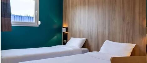 A hotel room with two beds, a window, a shower, and a bathroom with a sink.