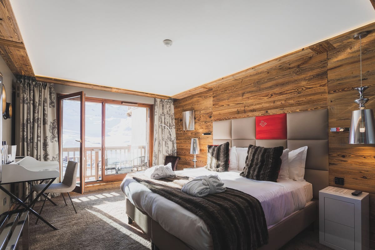 Una habitación de hotel moderna con techo de madera, una cama grande con muchas almohadas, un escritorio y una silla.