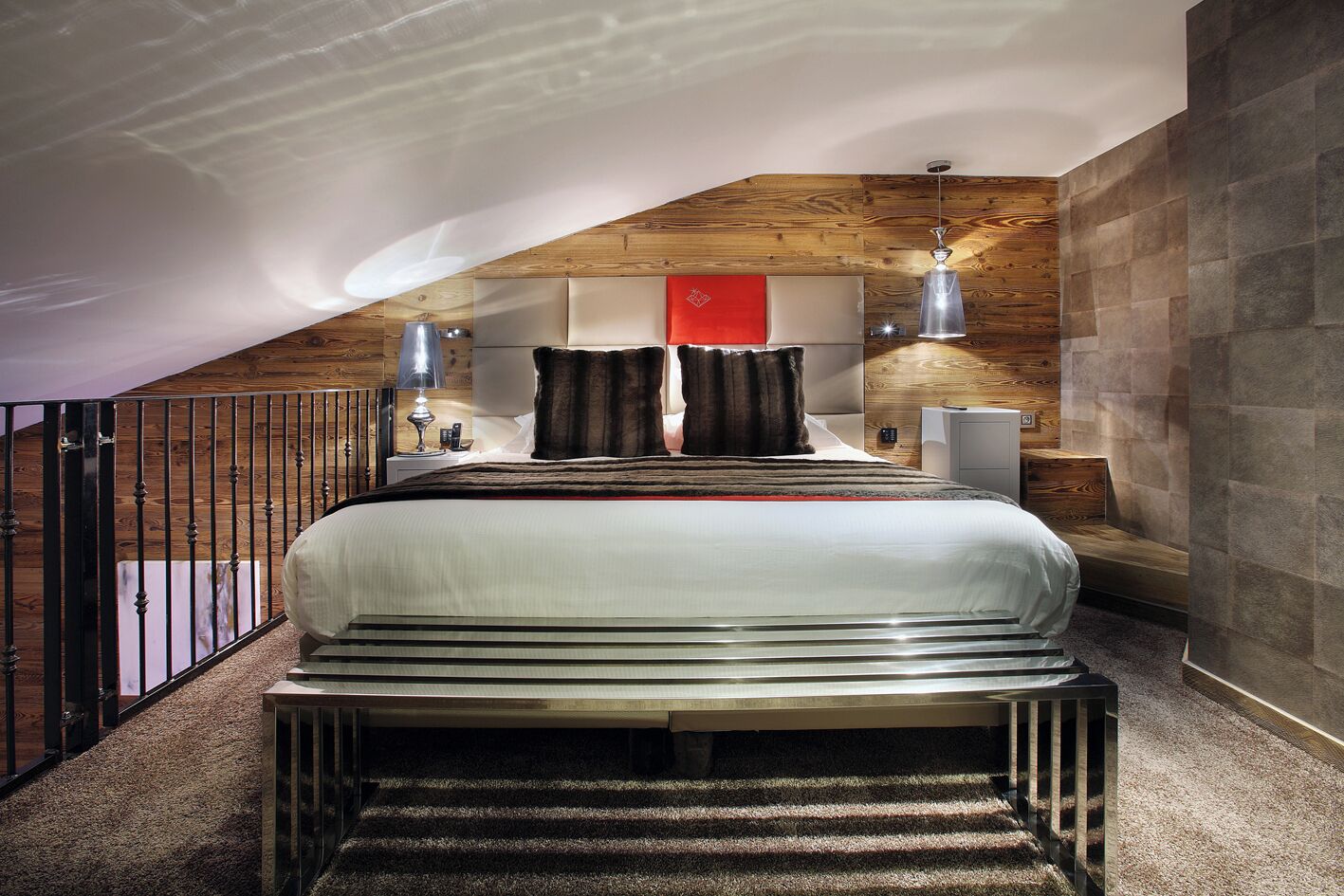 A modern bedroom with a large bed, a wooden ceiling, and a stone wall.