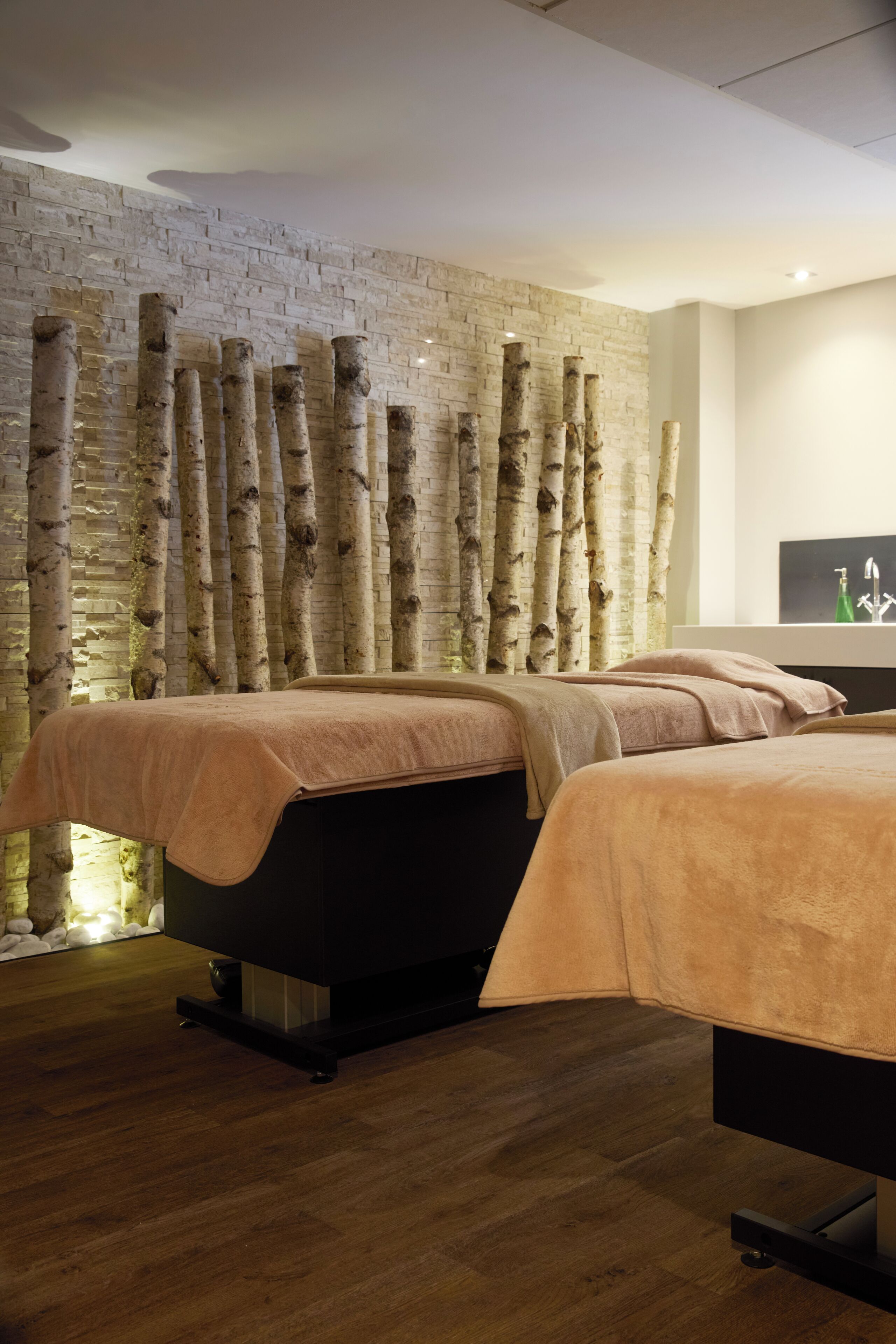 A modern bedroom with two beds, a brick wall, and a unique tree bark wall design.