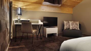 A hotel room with a wooden ceiling, a desk with a lamp, a television, a chair, a bed, and a sofa.
