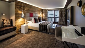 Quarto de hotel moderno com parede de destaque em madeira, uma cama grande, uma escrivaninha e vista para a paisagem nevada.