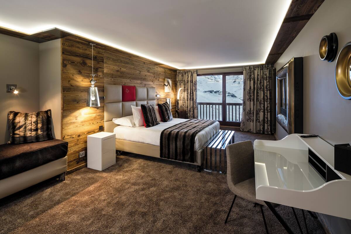Habitación de hotel moderna con un revestimiento de pared de madera, una cama grande, un escritorio y vistas al paisaje nevado.