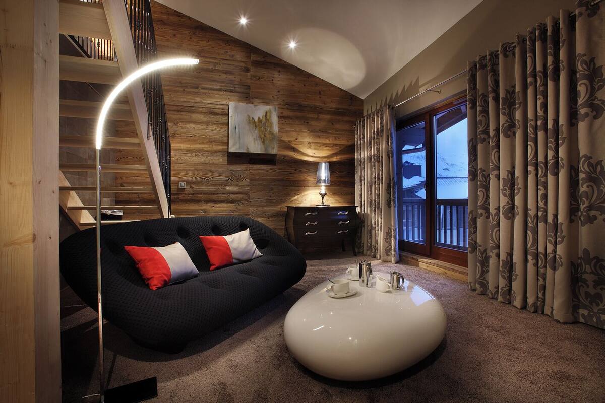 Una sala moderna con un sofá oscuro, una mesa de centro blanca y una escalera de madera.