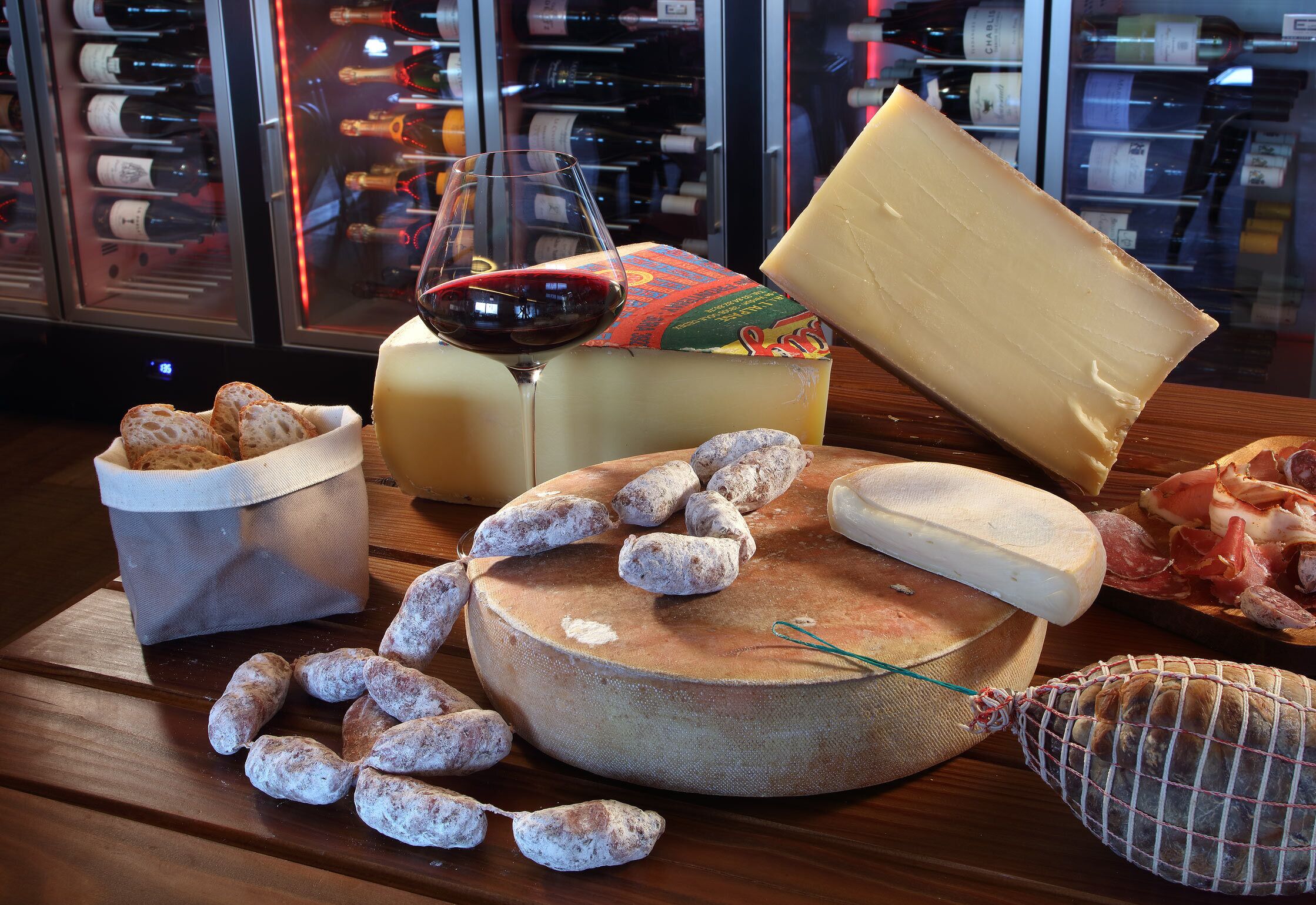 A cheese board with various cheeses, a glass of red wine, and some cured meats.