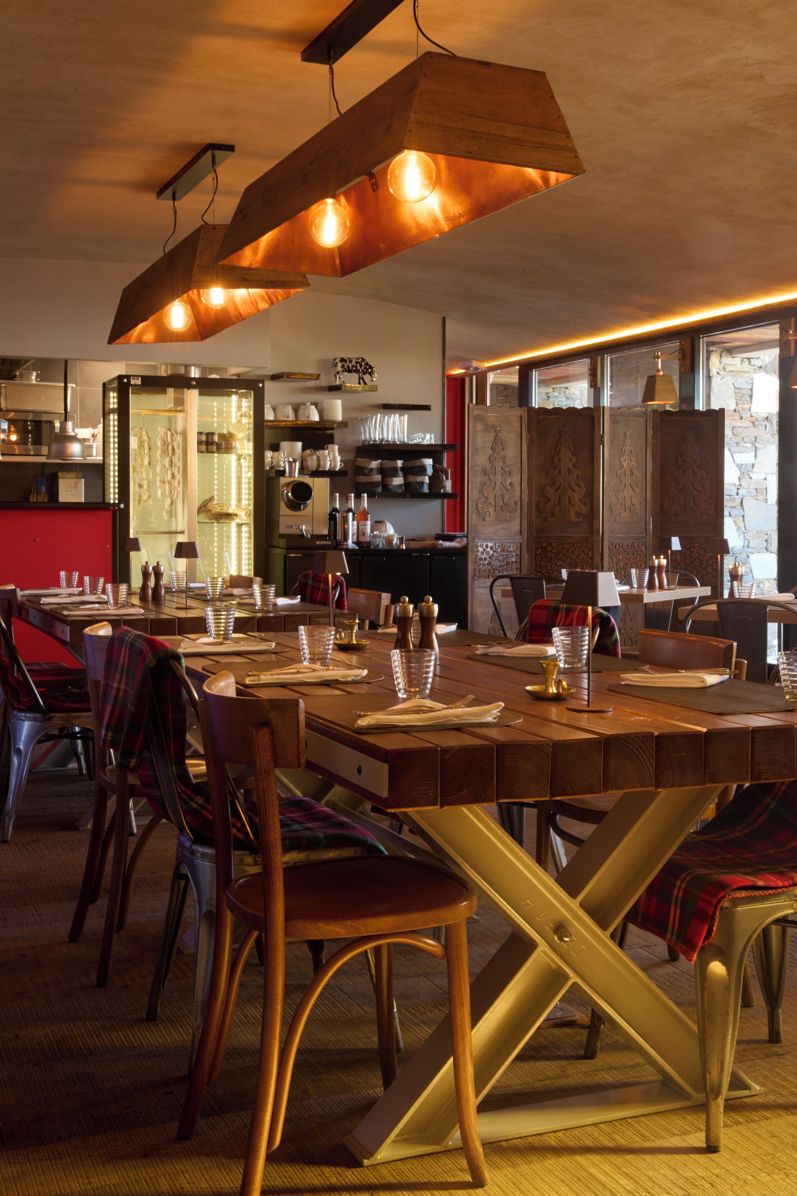 Ein Restaurant mit Holztischen und -stühlen, einer hängenden Leuchte und Blick auf den Küchenbereich.
