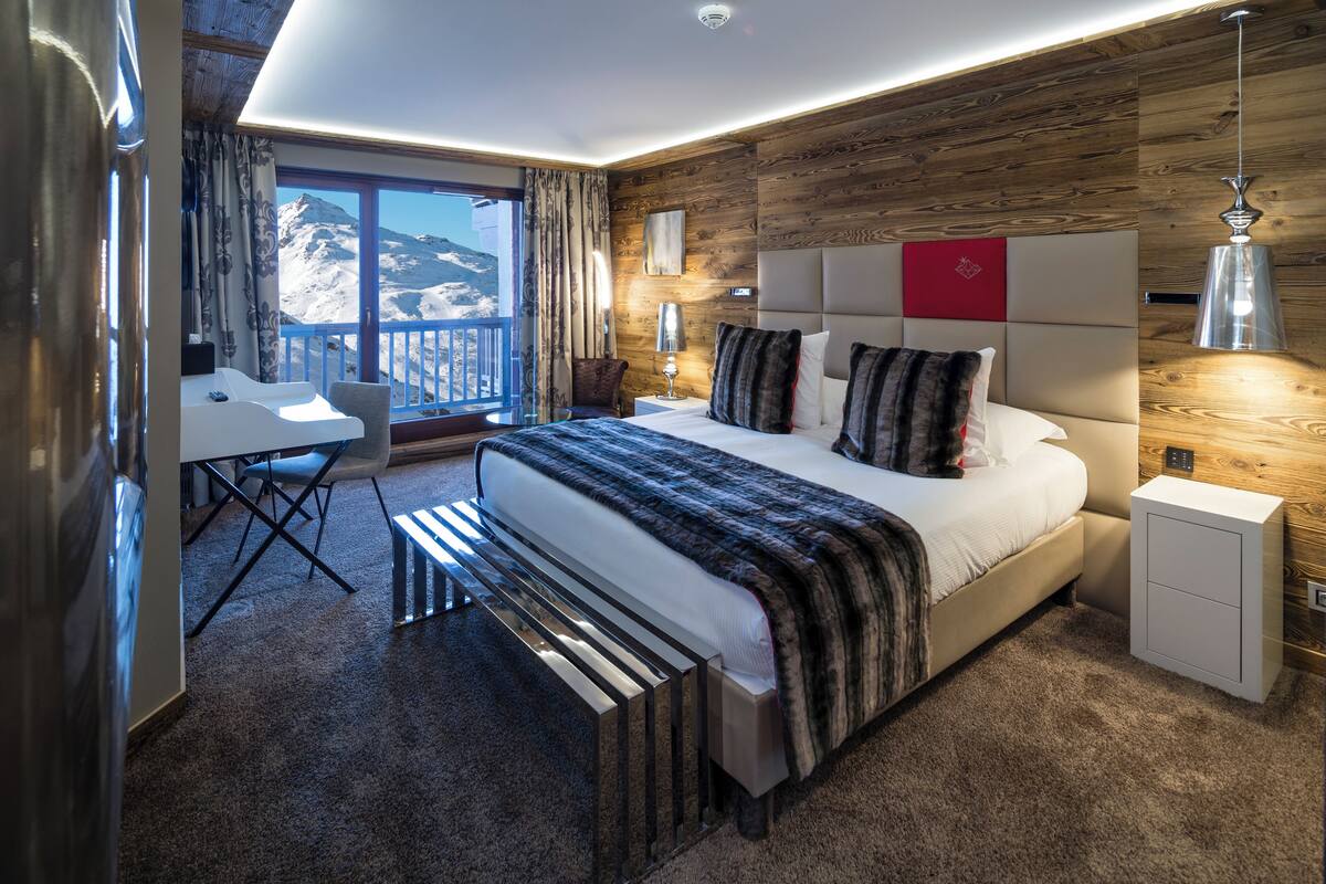 Una habitación de hotel moderna con una cama grande, un escritorio y vistas a montañas.