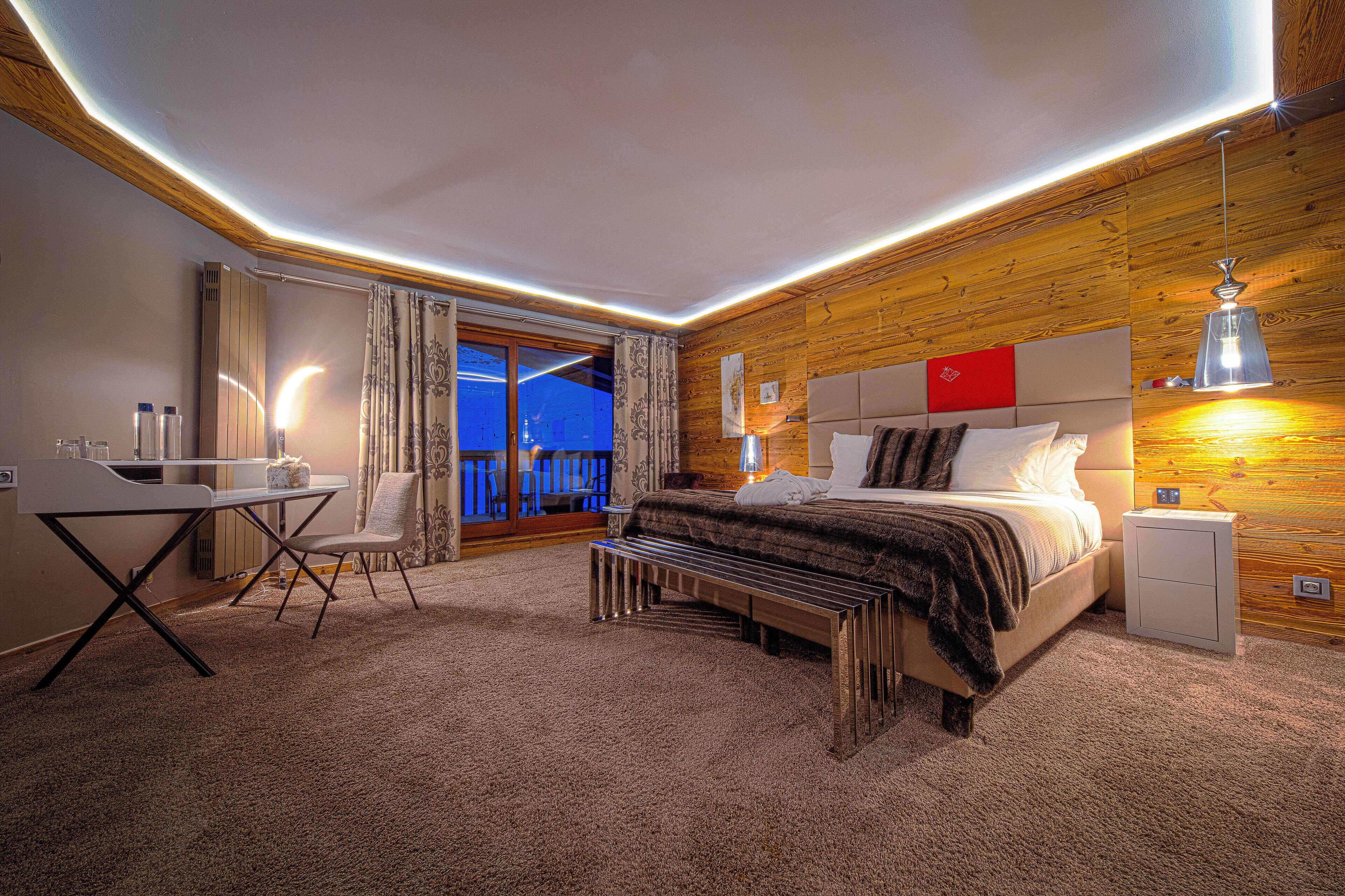 Une chambre moderne avec un plafond en bois, un lit doté d’une tête de lit rouge, un bureau et une chaise.