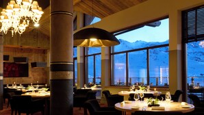 Um restaurante com vigas de madeira, amplas janelas e vista para as montanhas, e um candelabro.