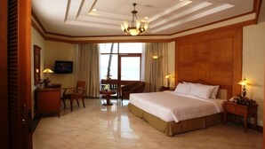 Habitación de hotel con una cama grande, un escritorio, una silla, un televisor y una ventana con cortinas.