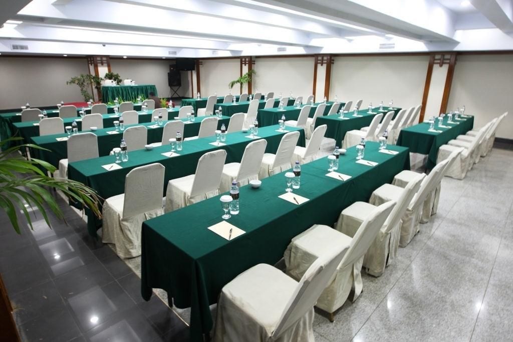 A conference room with rows of tables, each covered with a green tablecloth and white chairs.