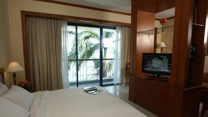 Habitación de hotel con una cama grande, un televisor sobre un mueble de madera y vistas a palmeras a través de la ventana.