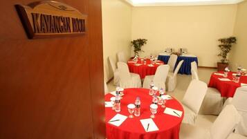 A conference room with round tables, each covered with a red tablecloth and white chairs.