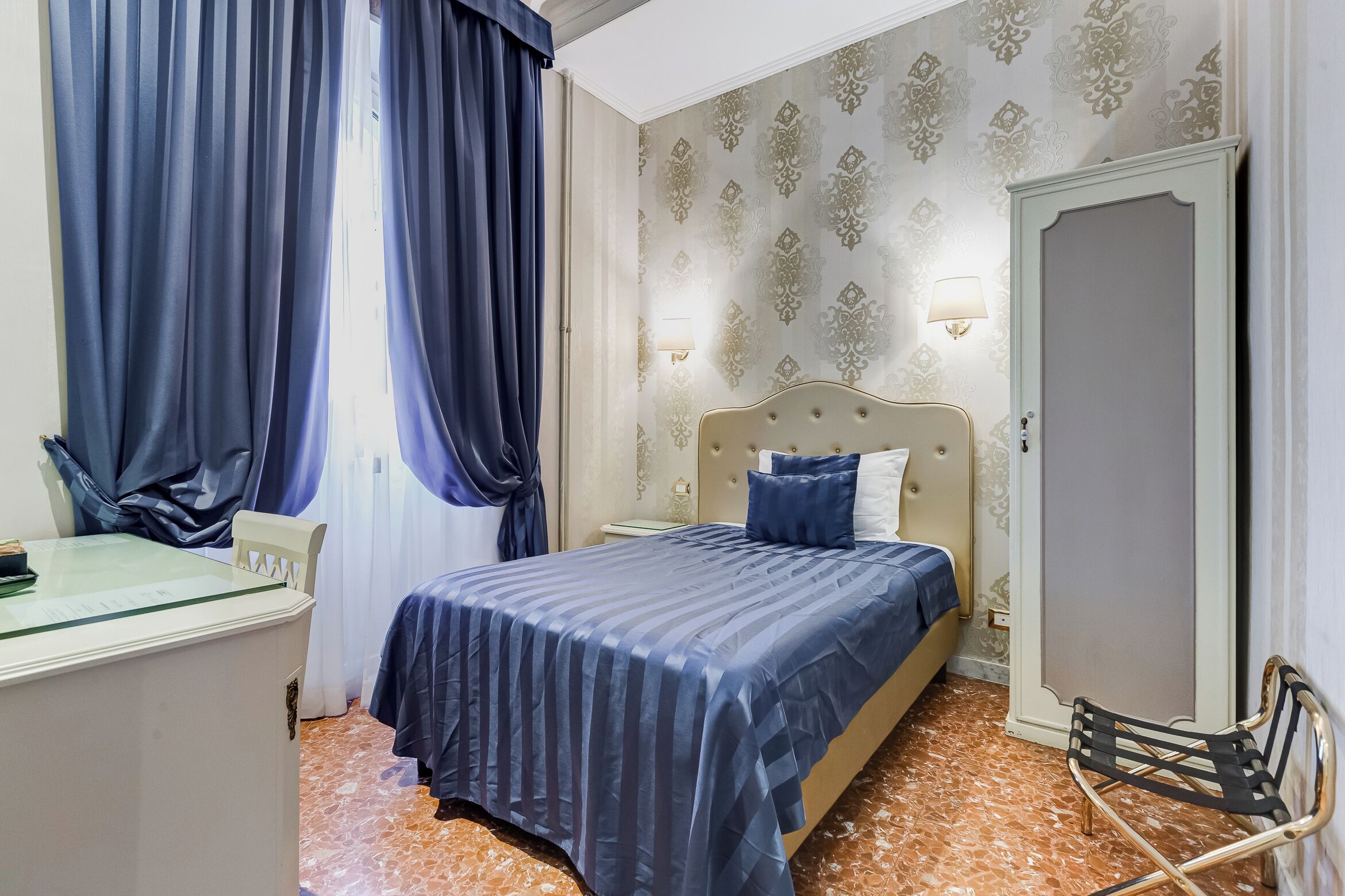 A hotel room with a bed, a desk, a chair, and a wardrobe.