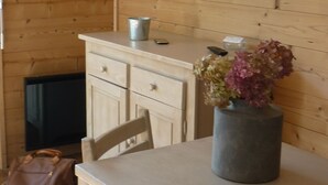 A wooden interior with a television mounted on the wall, a table with a vase of flowers, and a chair. - La Résidence (La Clusaz)
