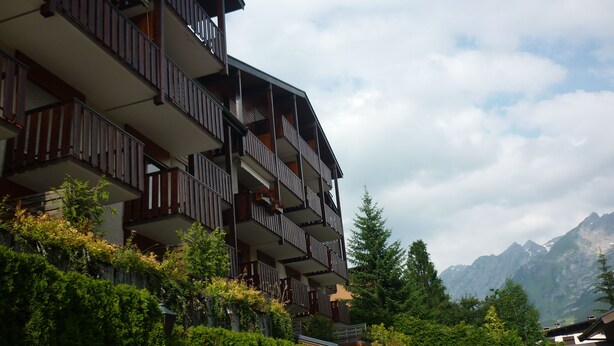 A multi-story building with balconies, surrounded by lush greenery and mountains in the background. - La Résidence (La Clusaz)