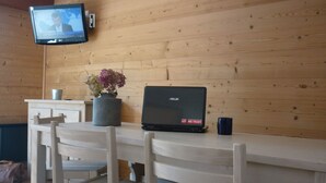 A wooden cabin interior with a wooden table, a laptop, a vase with flowers, a television, and a mug. - La Résidence (La Clusaz)