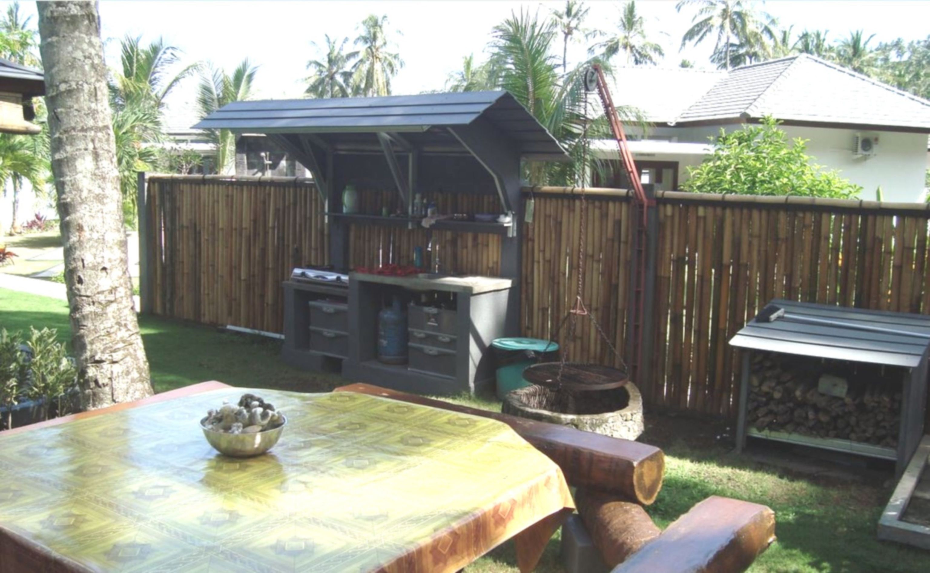 An outdoor kitchen area with a barbecue grill, a wooden table with a bowl, and a wooden bench.