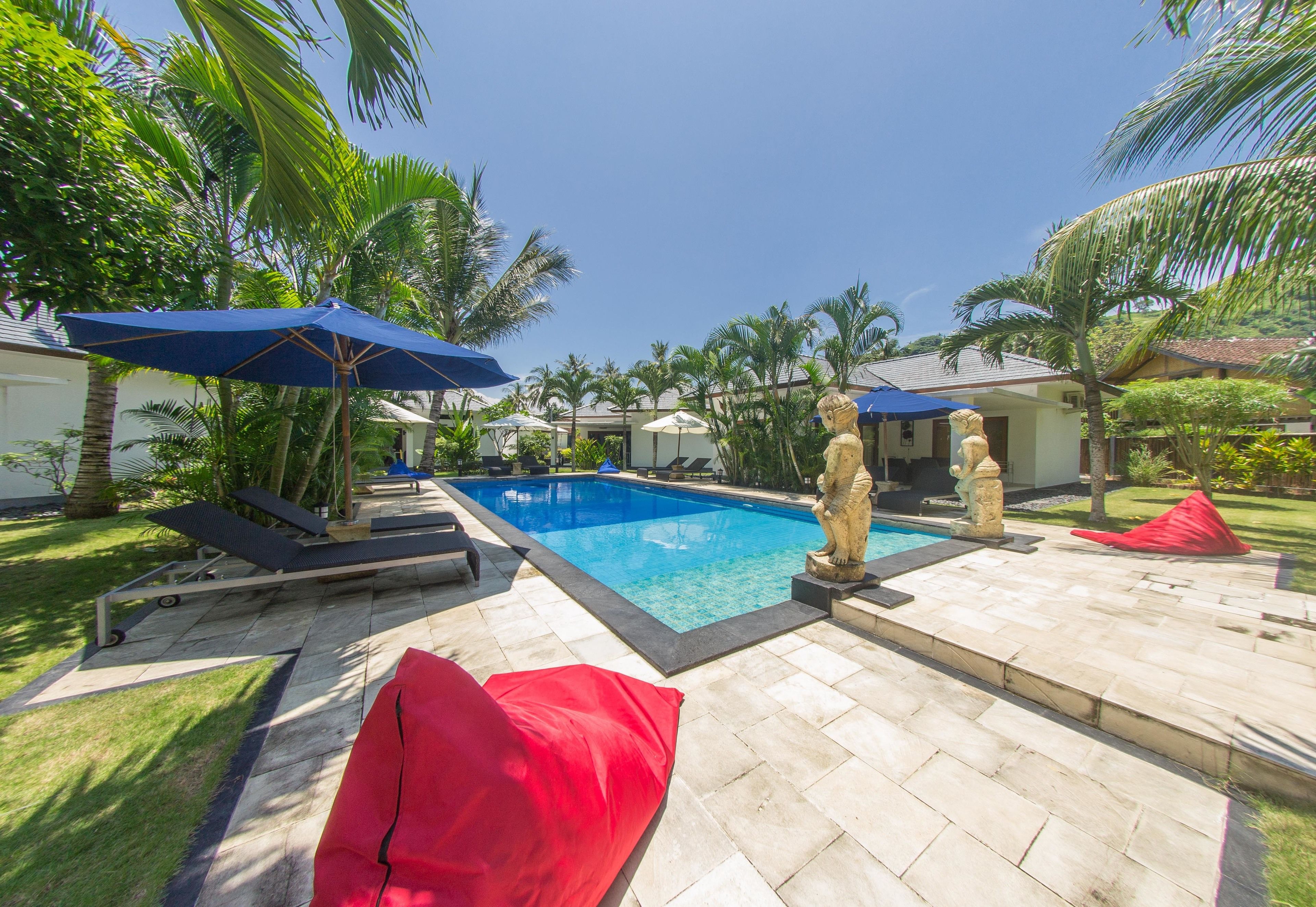 A swimming pool with lounge chairs and umbrellas, surrounded by palm trees and a well-maintained lawn.