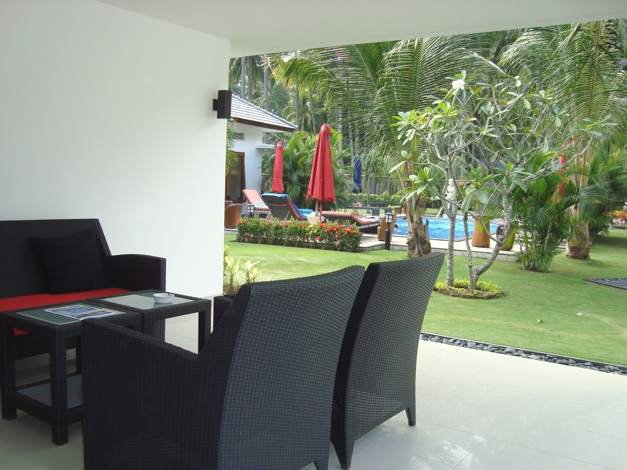A modern outdoor seating area with a glass table and chairs, overlooking a pool and lush greenery.
