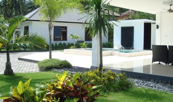Una casa moderna con piscina, rodeada de exuberante vegetación y palmeras.