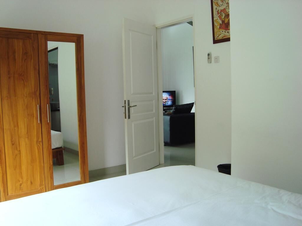 A bedroom with a wooden wardrobe, a white door, a bed, and a television in the background.