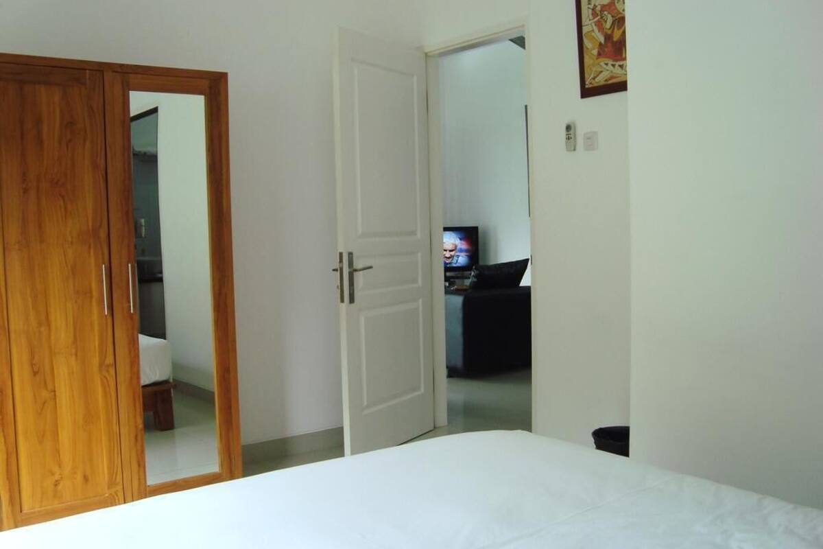 A bedroom with a wooden wardrobe, a white door, a bed, and a television in the background.
