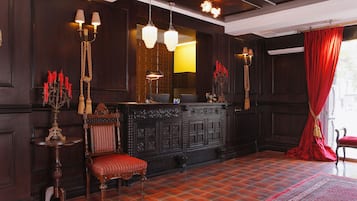 Una habitación con paneles de madera oscura, un sillón tapizado en rojo, un escritorio de madera con espejo y una cortina roja.