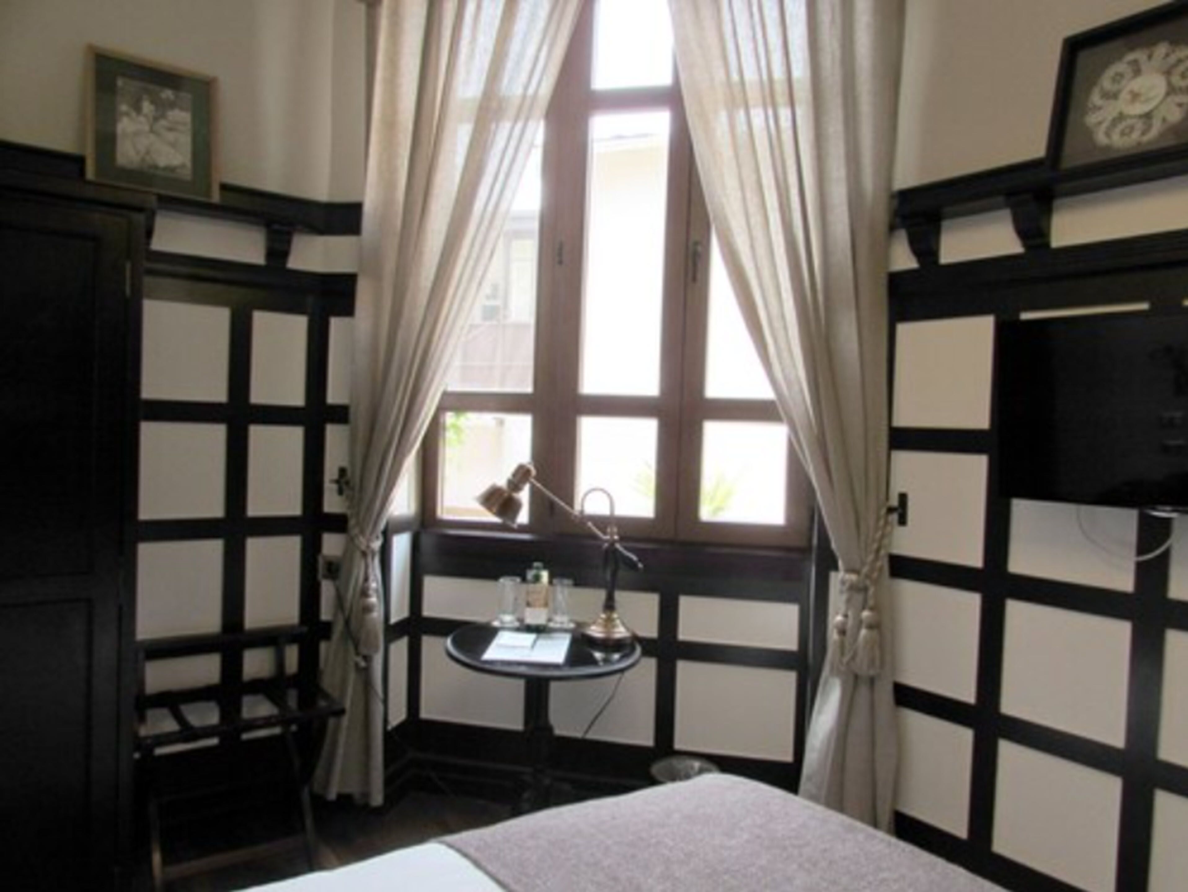 A room with a bed, a desk with a lamp, and a window with curtains.